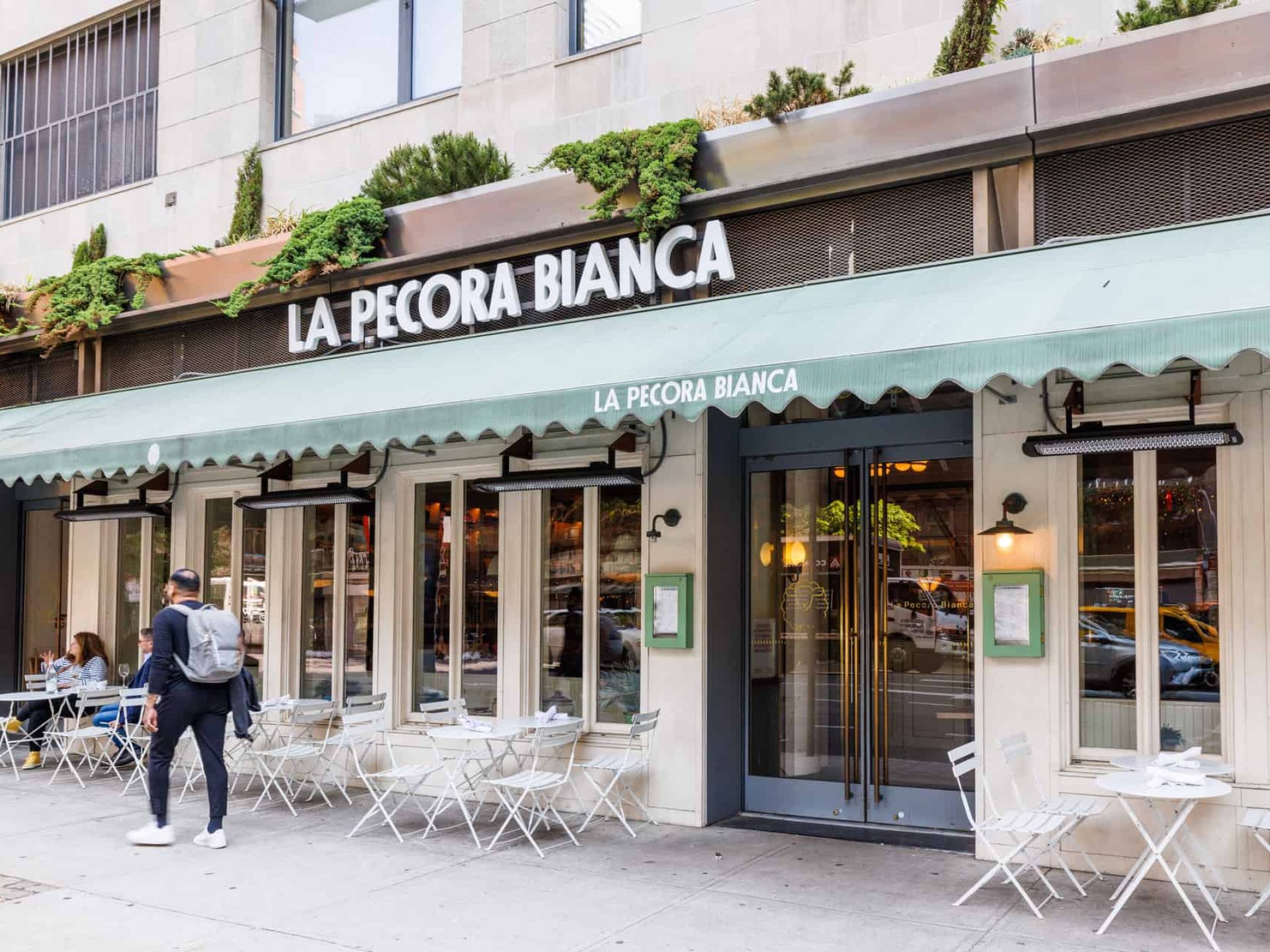 Entrance to La Pecora Bianca. Double doors covered by a green awning across the front of the building and tall windows.