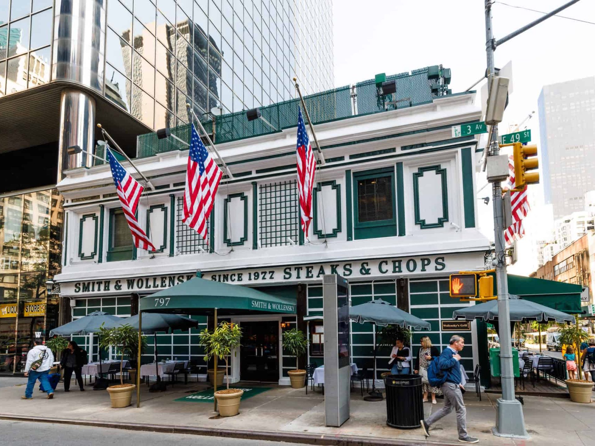 Exterior of Smith & Wollensky Steakhouse. White building with a green awning over the front door and outdoor seating.